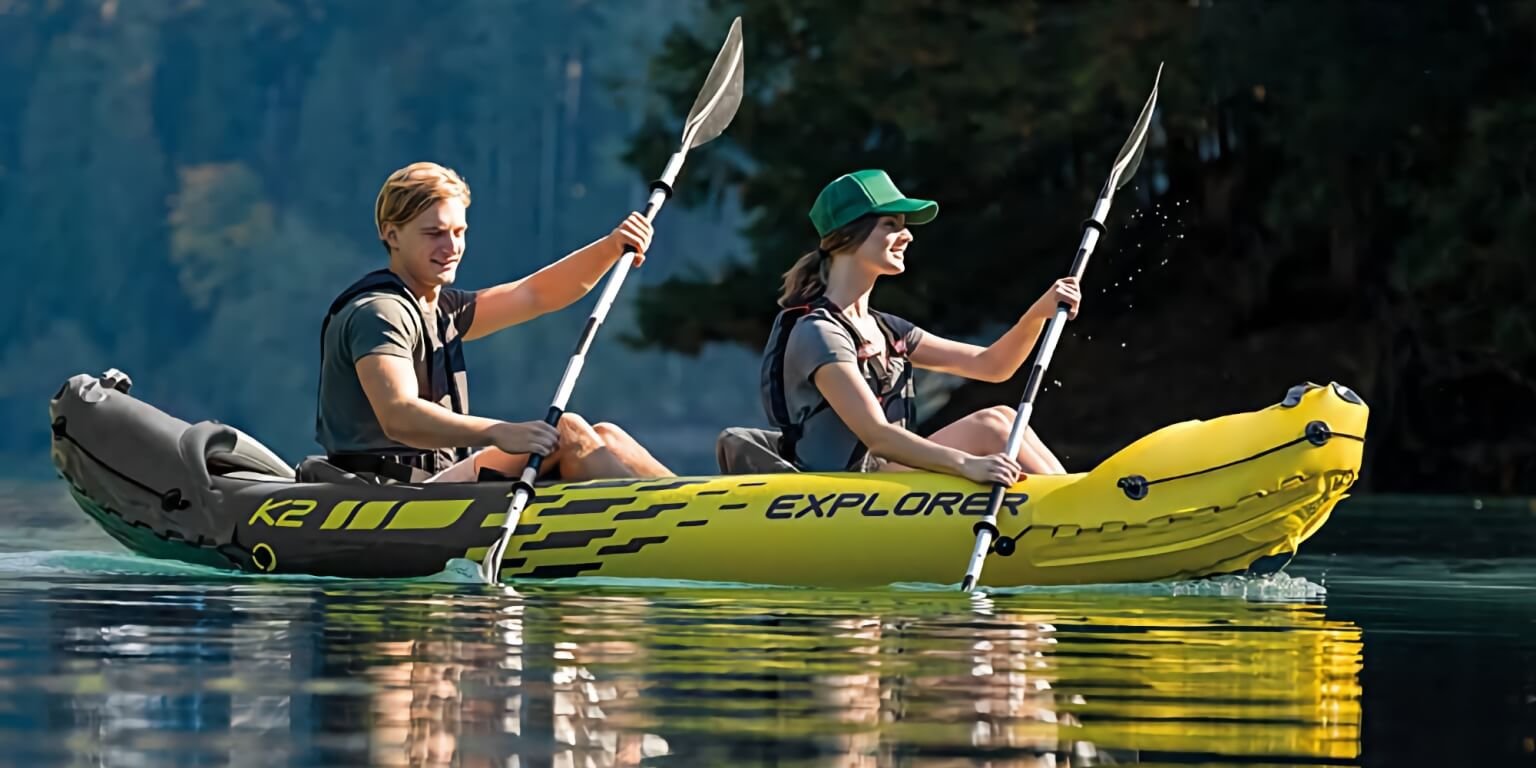 Un jeune homme et une jeune femme pagayant sur un canoÃ« gonflable Intex. Le kayak gonflable est jaune et gris.