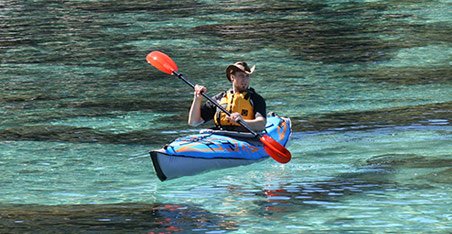 Homme naviguant sur canoé kayak gonflable bleu au milieu d'une eau turquoise