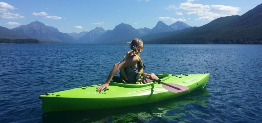 Jeune femme blonde dans un kayak gonflable sur un lac au milieu des montagnes